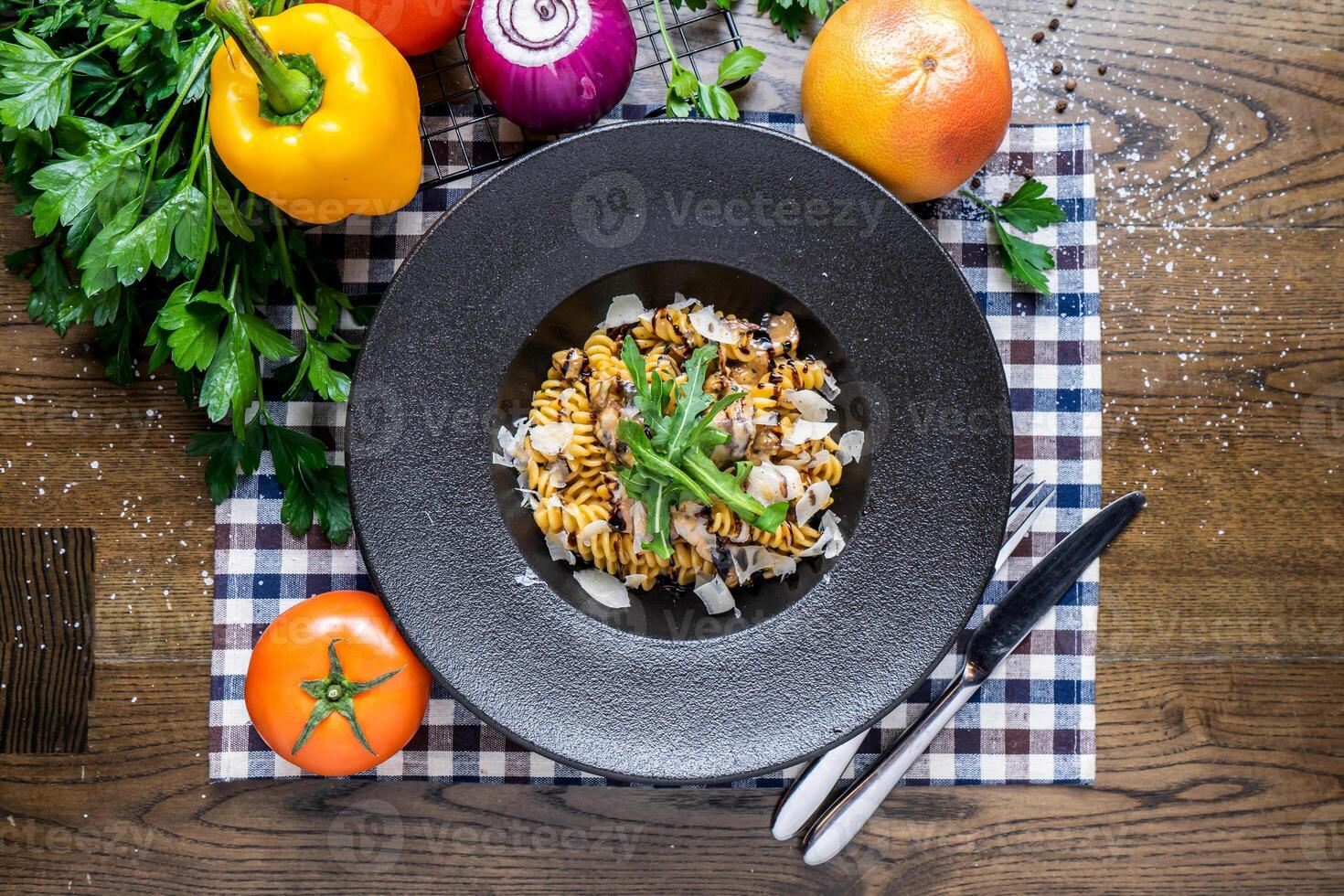 Porcini Fusilli with herbs, tomato, onion, capsicum, coriander, knife and fork served in dish isolated on napkin top view of italian fastfood on wooden table photo