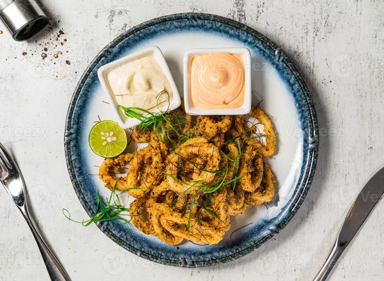 Fried Calamari or Flashed fried squid rings with lemon mayo dip sauce served in plate isolated on background top view of italian food photo