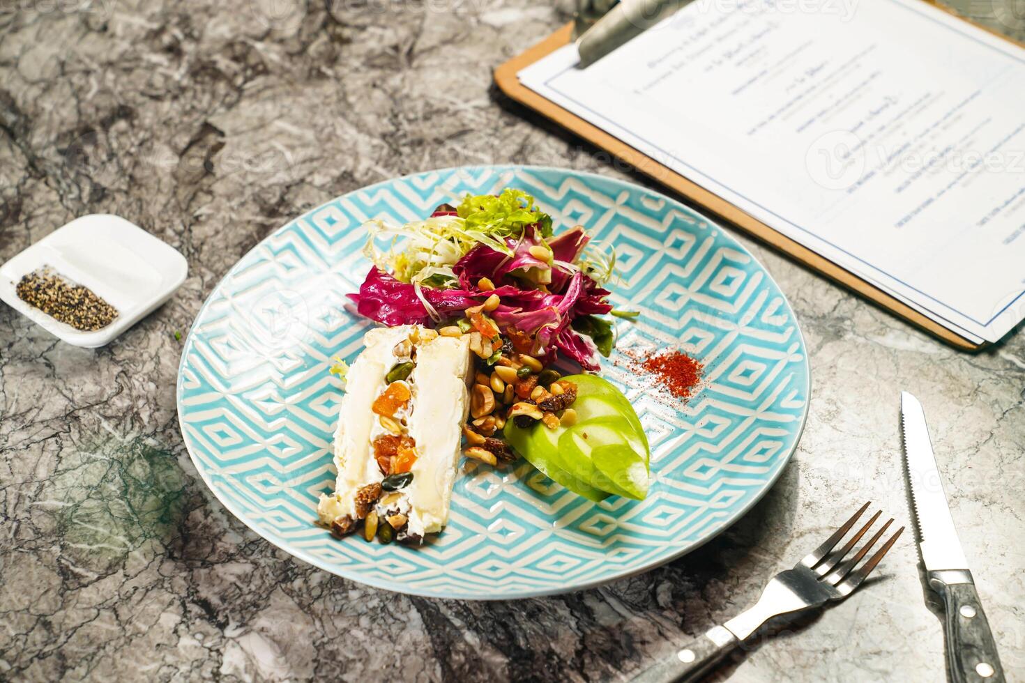 Brie cheese with dried fruit and apple and celery garden salad with dip, fork and knife served in plate isolated on marble background side view of hong kong food photo