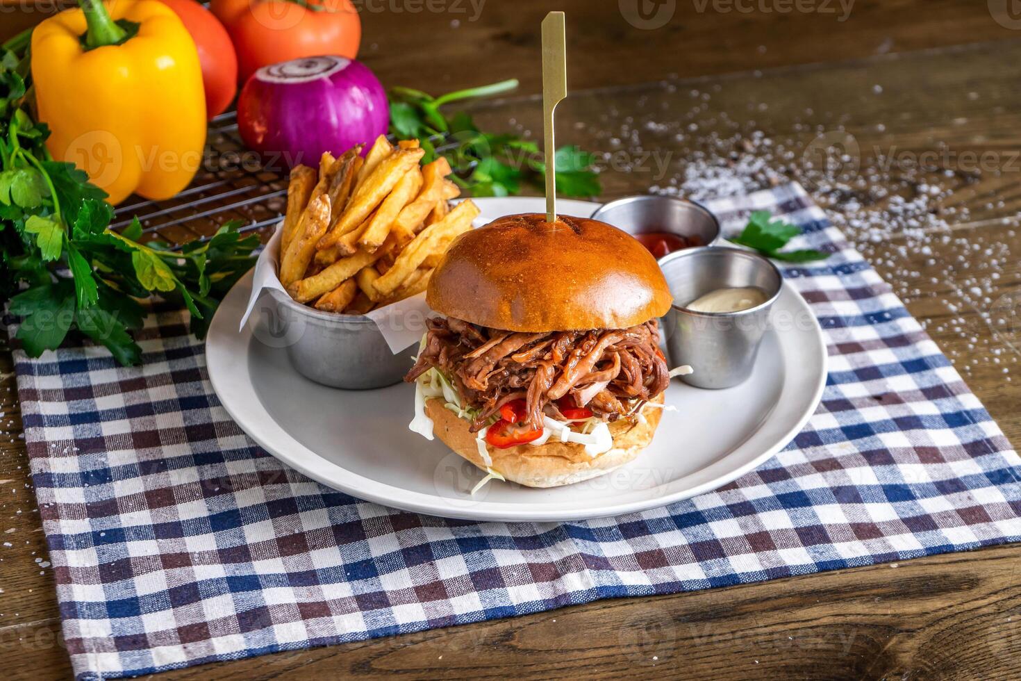 Pulled Pork Burger with french fries, ketchup, mayo dip, tomato, onion, capsicum, coriander, served in dish isolated on napkin side view of italian fastfood on wooden table photo