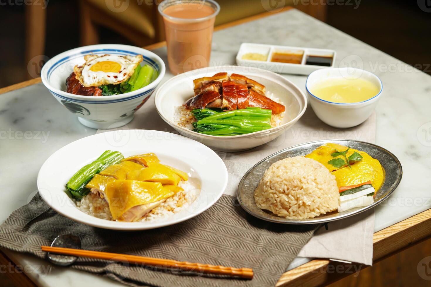 Boneless Hainanese Chicken Rice, Roasted Duck, Poached Chicken, BBQ Pork with Fried Egg, baby kailan, milk kopi and chopsticks isolated on napkin table side view of assorted asian foods photo