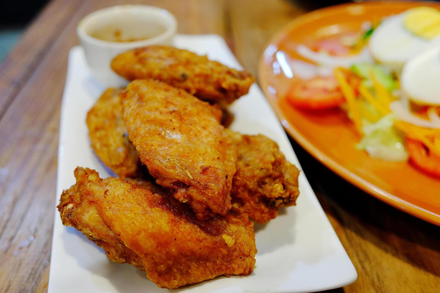 Fried chicken wings and dipping sauce on white plate with vegetable salad with boiled eggs and mayonnaise sauce photo