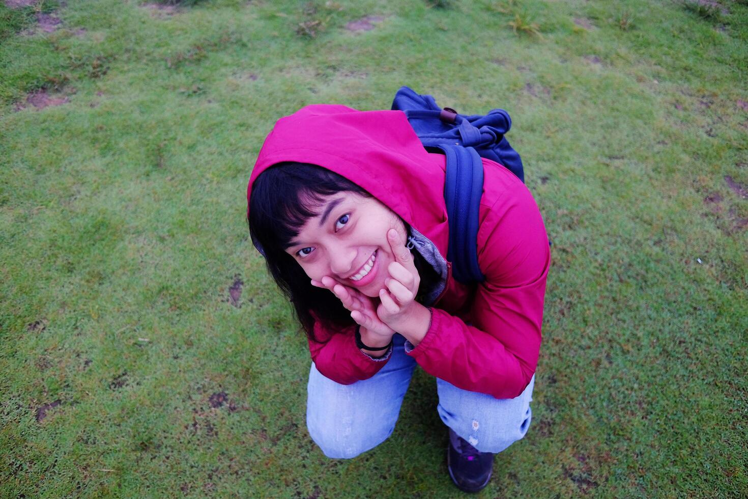 Asian young woman in red raincoat and bag sitting on green grass field and foggy with mist on mountain in rainy season. Travel in Asian photo
