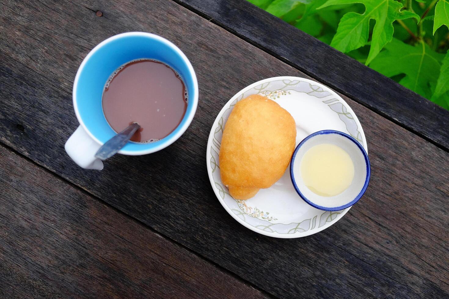 Yang fried dumpling or Bread fried bun recipe with sweetened condensed milk in a bowl and a cup of hot chocolate on wooden table in tropical garden. Asain Breakfast in Thailand photo