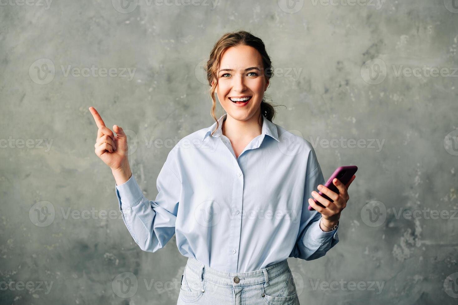 Cheerful young woman with a smartphone, enthusiastically showcasing a mobile app. Perfect for business, tech, or app promotion imagery. Isolated on a neutral background. Ideal for ads and web services photo