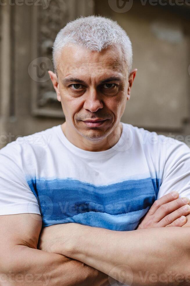 A man with a blue and white shirt is standing with his arms crossed photo