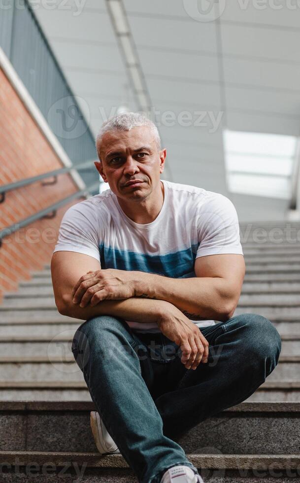 A man in a white and blue striped shirt sits on a set of stairs photo