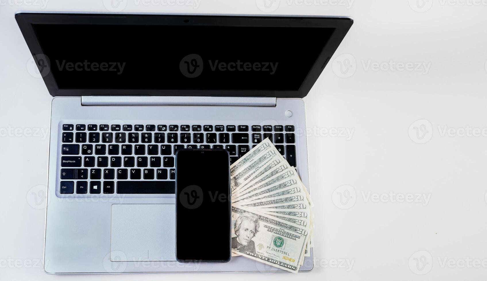Top view of laptop with cell phone and dollar bills. Cell phone on laptop keyboard and dollar bills. Mobile phone on top of dollar bills on laptop keyboard photo