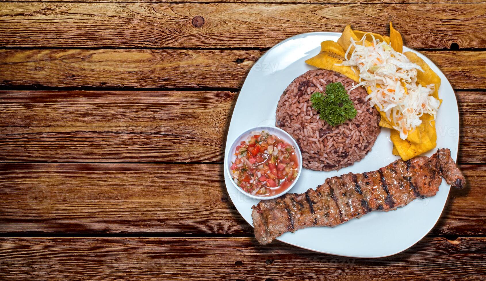 Roast beef dish with gallo pinto and pico de gallo, Roast beef with tomato and gallo pinto salad served on a wooden table, Plate with roast beef and rice served on a wooden table, Nicaraguan food photo