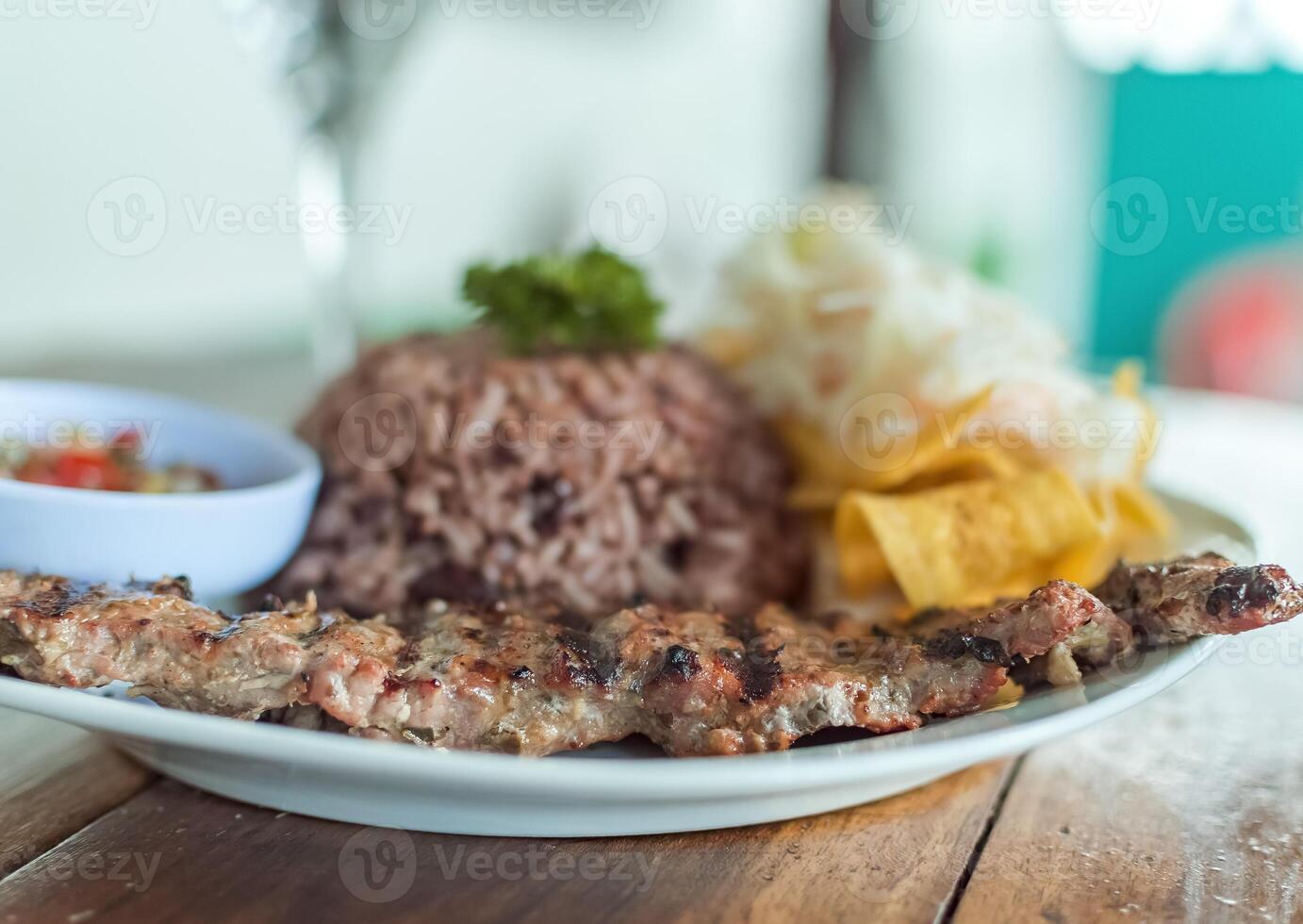 Close up of roast beef with gallo pinto and pico de gallo, Nicaraguan food served on wooden table, Plate with roast beef and rice served on wooden table photo
