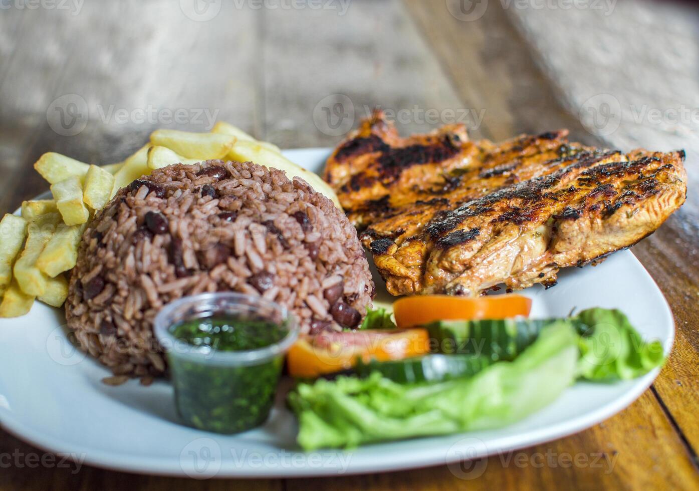 Close up of roasted chicken with gallo pinto and pico de gallo, Nicaraguan food served on wooden background, Plate with roast chicken and rice served on wooden background photo