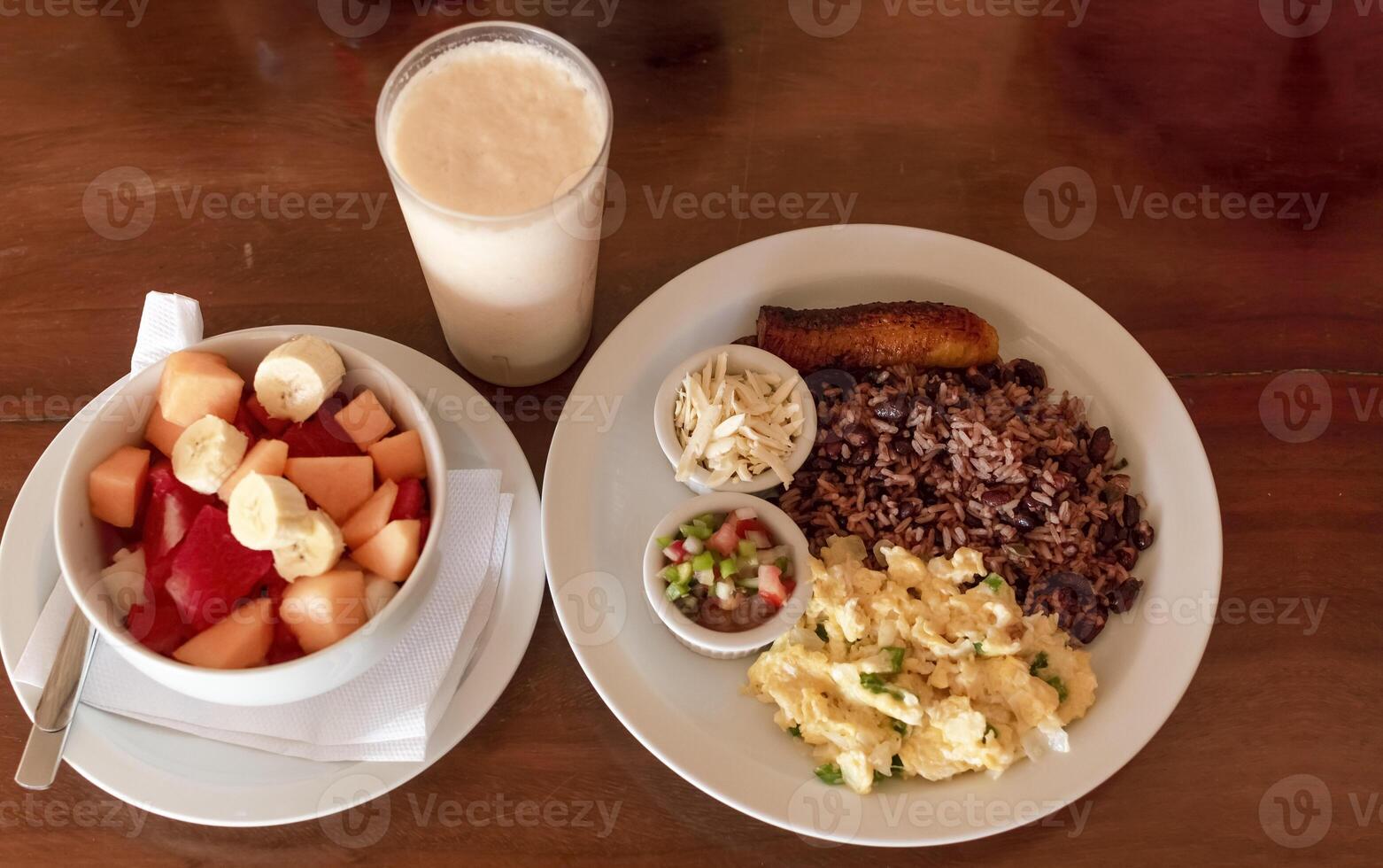 Gallo pinto breakfast served on the table with a fruit salad, Traditional gallopinto dish with fried eggs and a bowl of fruit salad on the table. Traditional gallo pinto served at the table photo