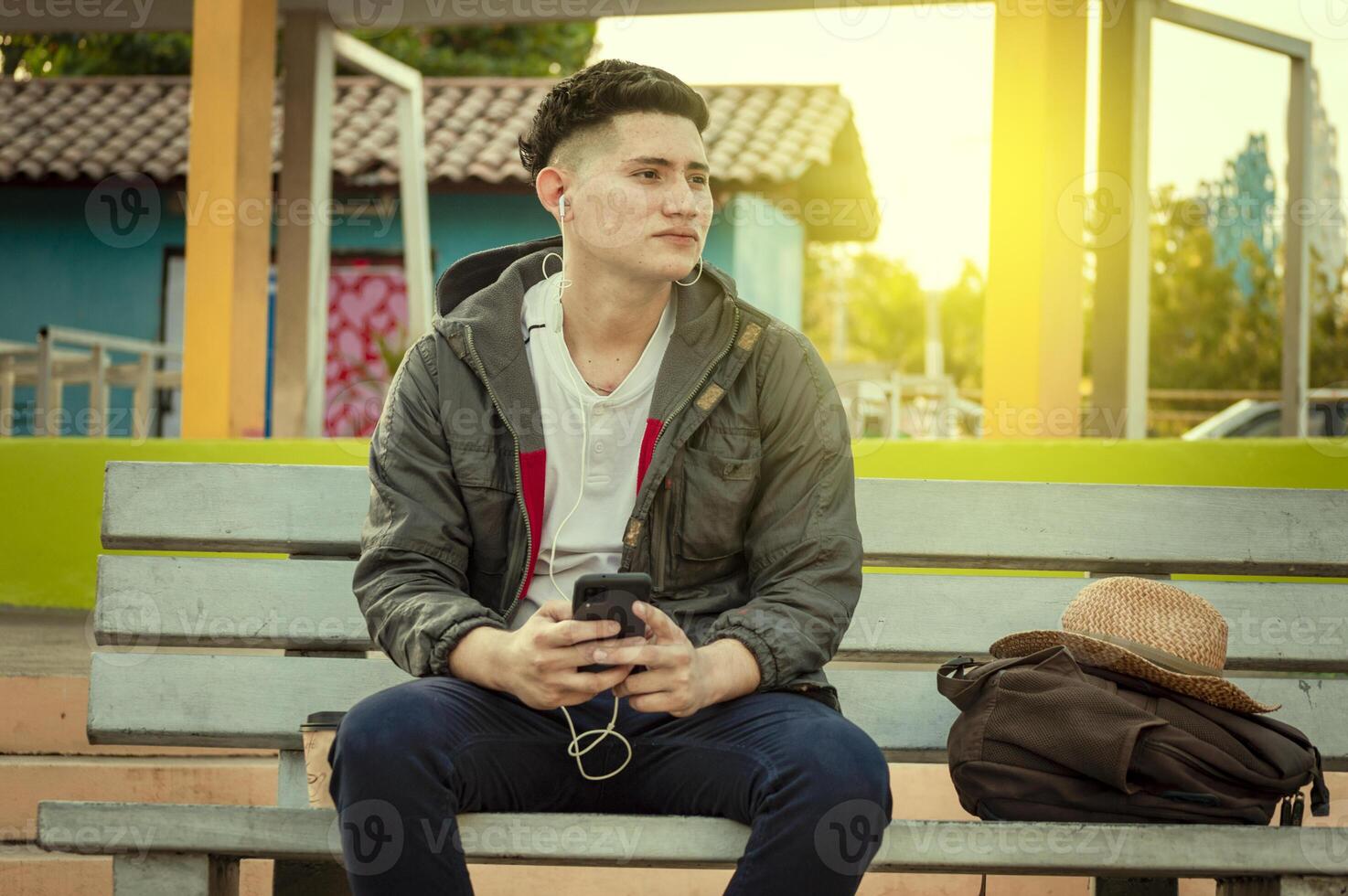 Attractive guy listening to music on a bench. Handsome man sitting on a bench listening to music with phone photo
