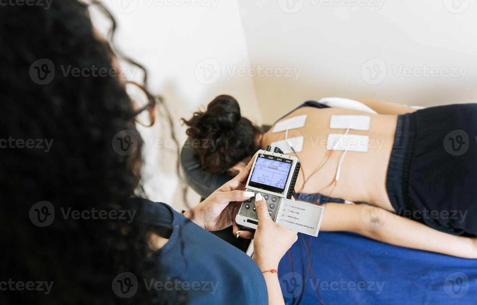 View of physiotherapist electrostimulating a patient. Lower back therapy with electrode pads. Electrode treatment to patient lying down, Professional physiotherapist electrostimulating patient photo