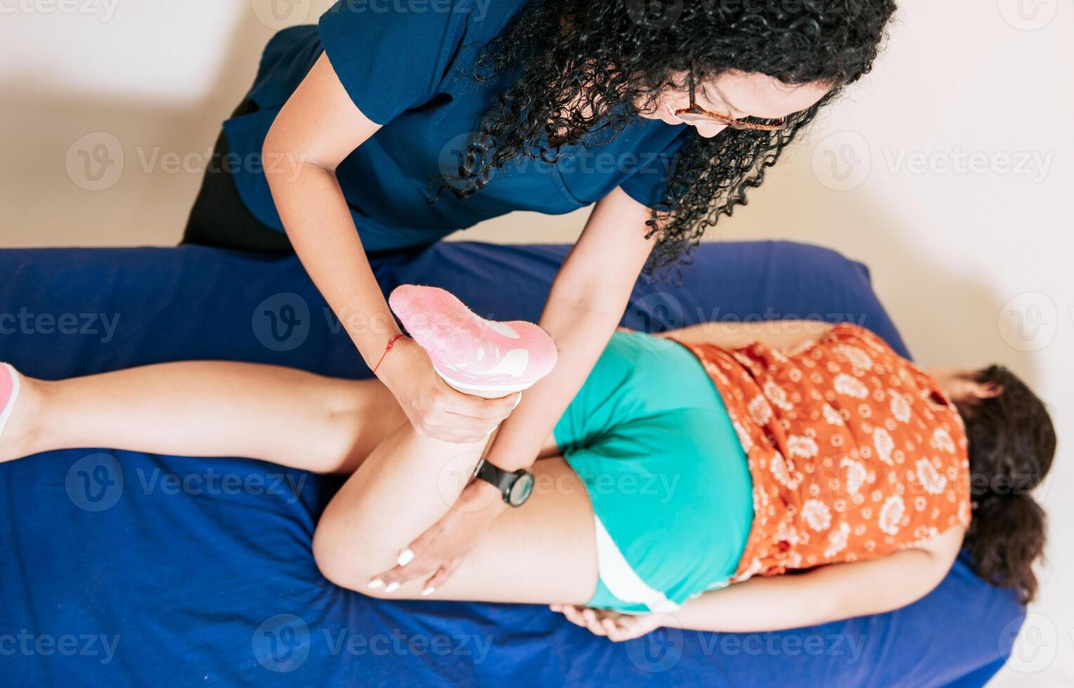 Top view of Chiropractor stretching knee to lying female patient, Knee flexion physiotherapy to female patient. Physiotherapist woman assisting knee to lying patient photo