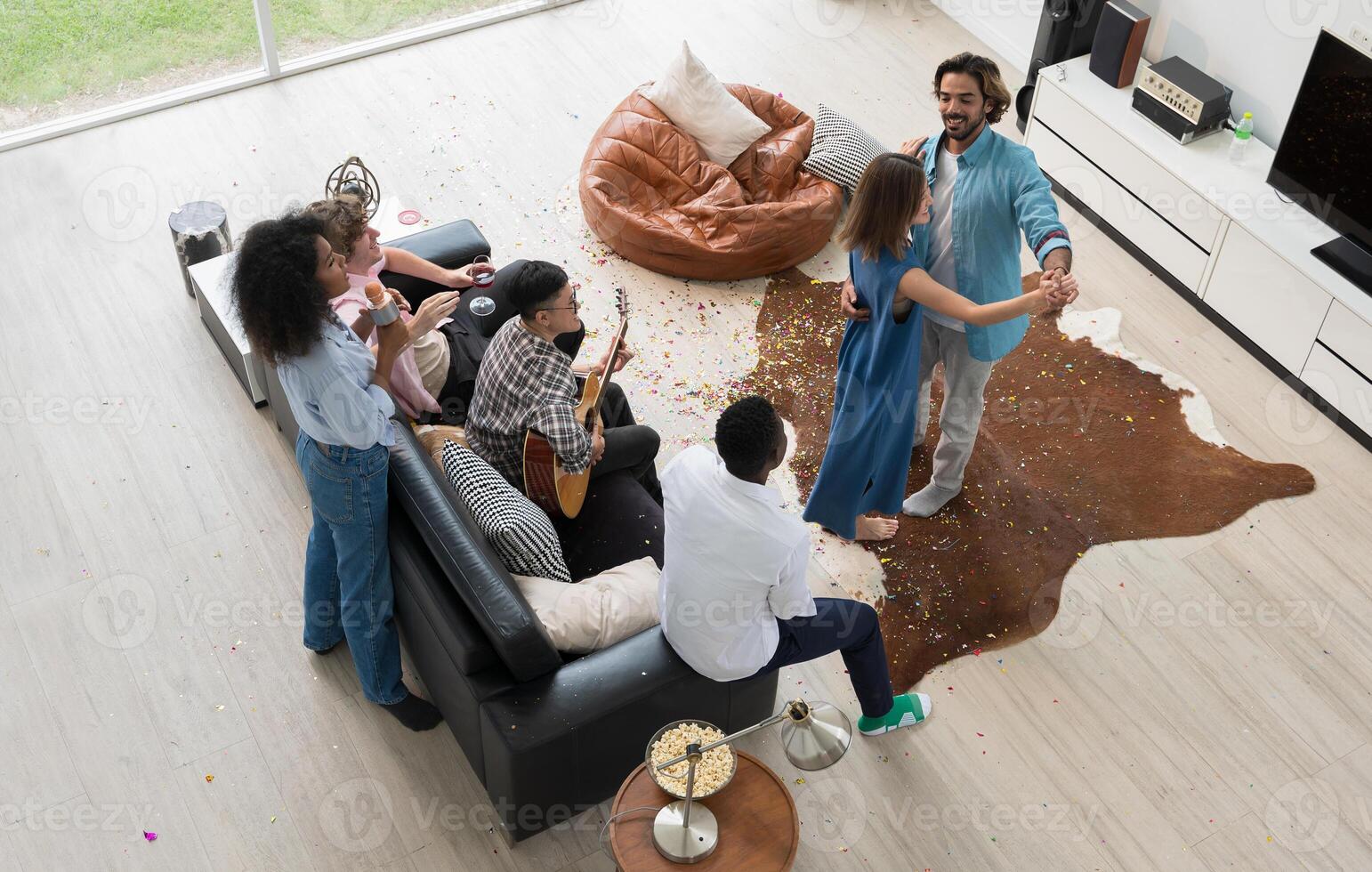 Group of diversity friends enjoys lively gathering in modern living room. Some sing, others play guitar and couple dances on celebration party at home photo