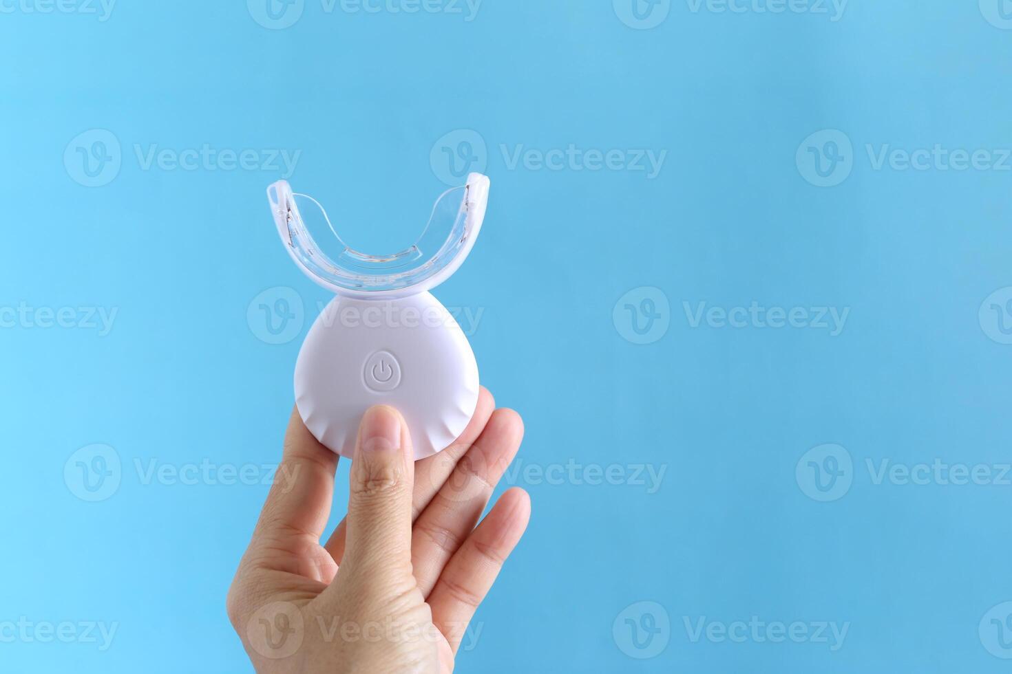 Home whitening, Closeup of woman holding LED light for whitening teeth on blue background, Healthy teeth and Tooth hygiene concept photo