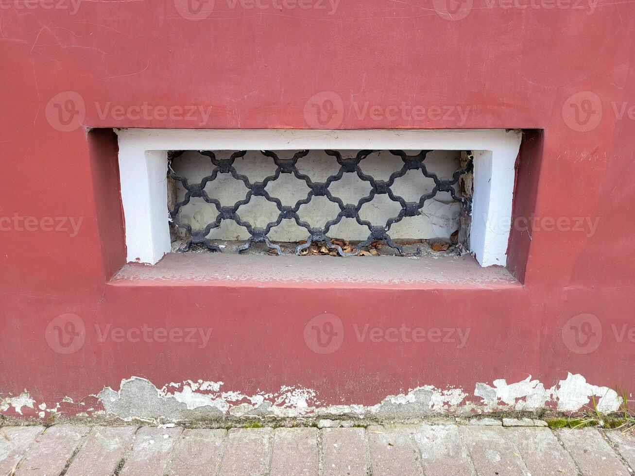 There is a small rectangular window with a wrought iron grille on the red facade of the house photo