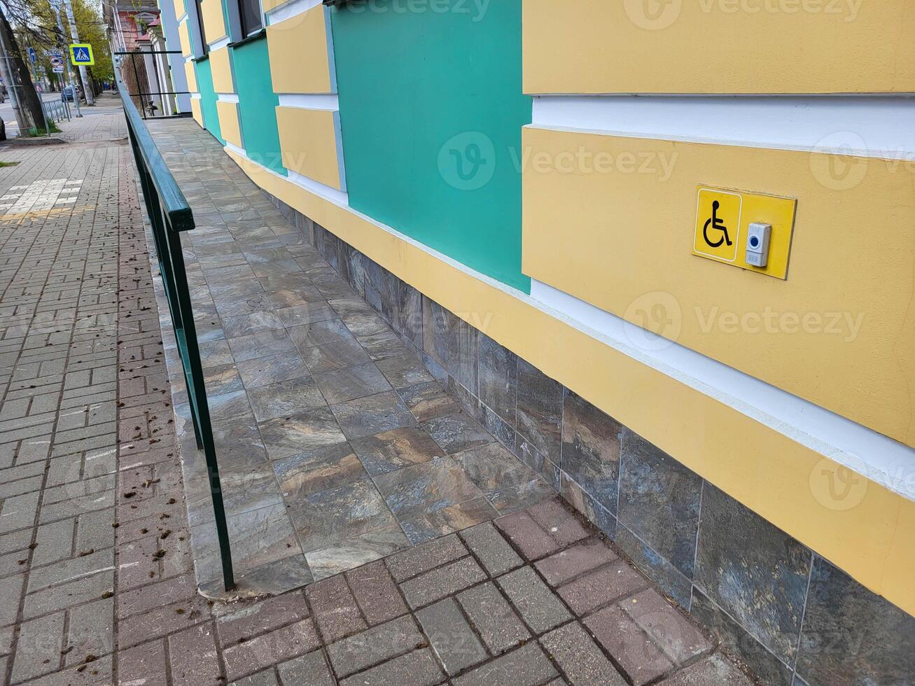 Yellow turquoise facade of the house with a lift and fences for people with wheelchairs and a sign with a call button photo