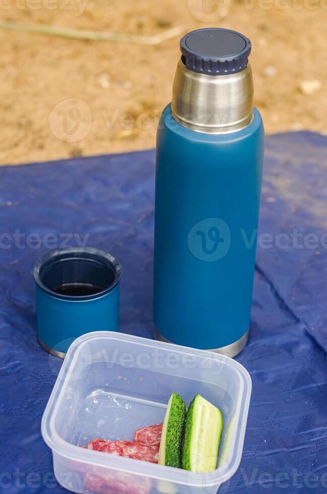 blue thermos with opened cup and plastic container with cucumber and sausage. High quality photo