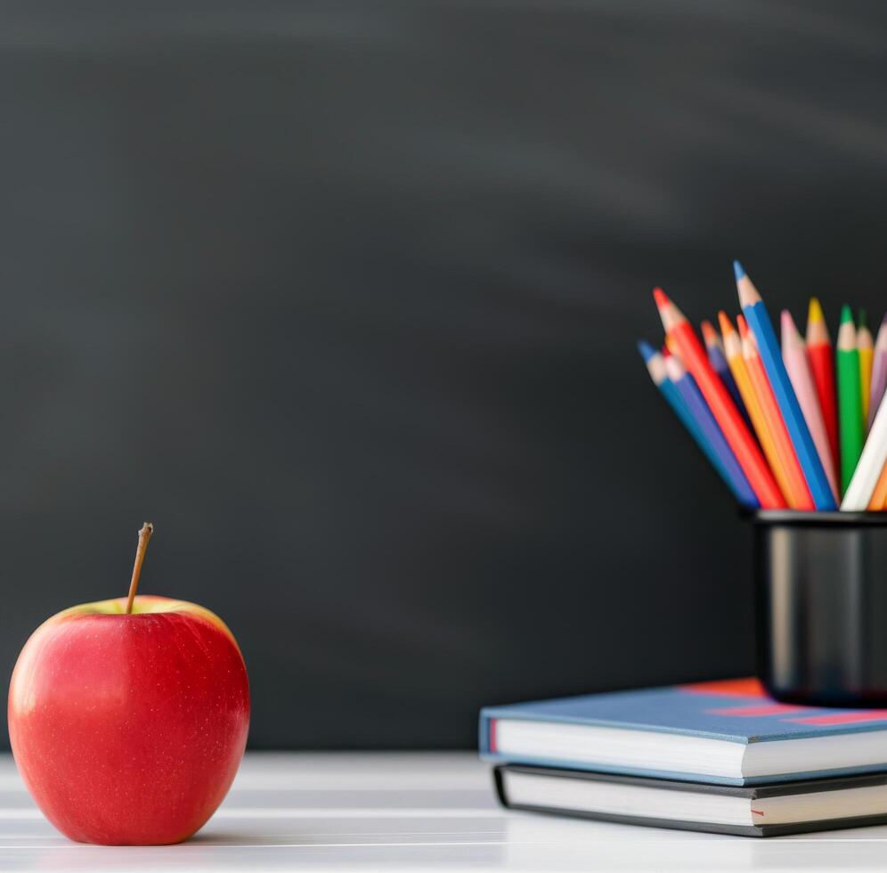 Colorful Pencils and Red Apple on Stacked Books Before Chalkboard photo