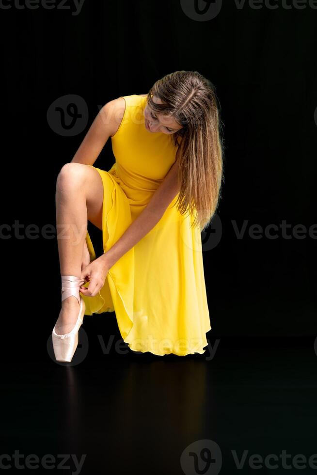 ballerina lacing her shoes, portrait on a black background photo