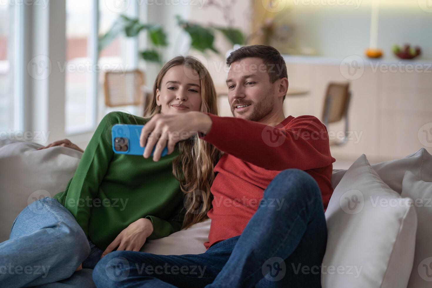 Pleased couple in love take selfies together for social media on cellphone at home capturing moment. photo