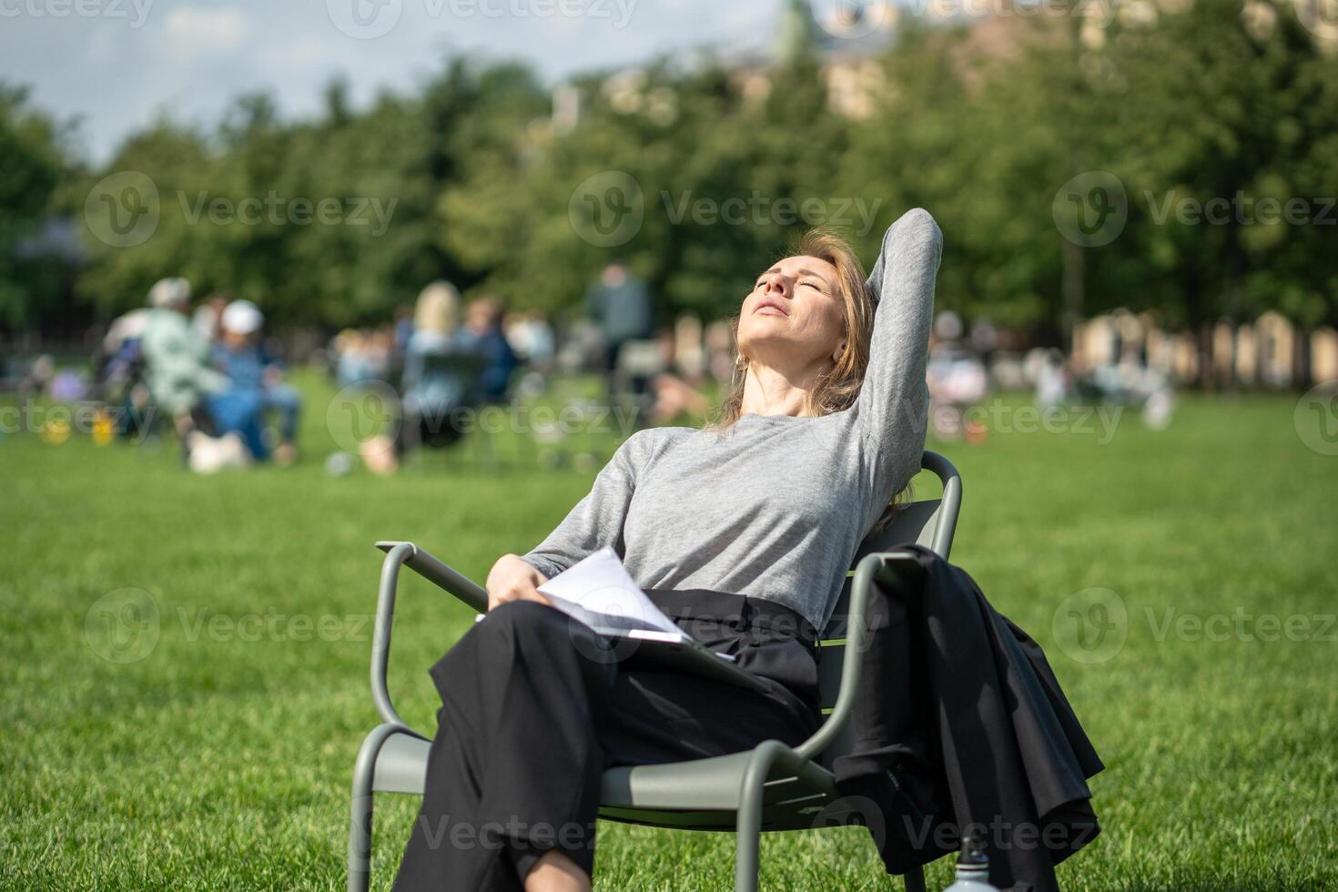 Relaxed woman rest on urban chair on lawn takes break from remote work enjoying sun with closed eyes photo