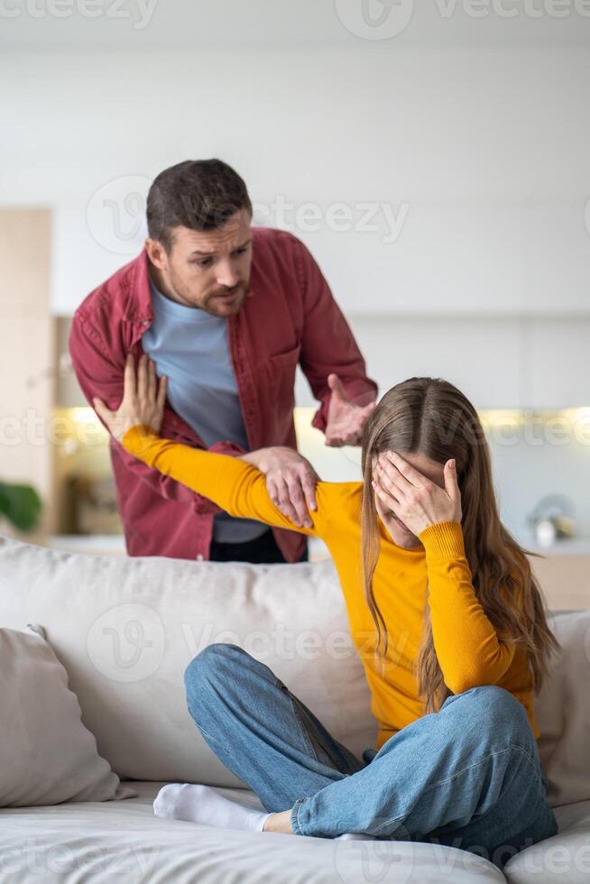 Tearful woman concealing face in hand and signaling to halt man who yelling and waving hands at home photo
