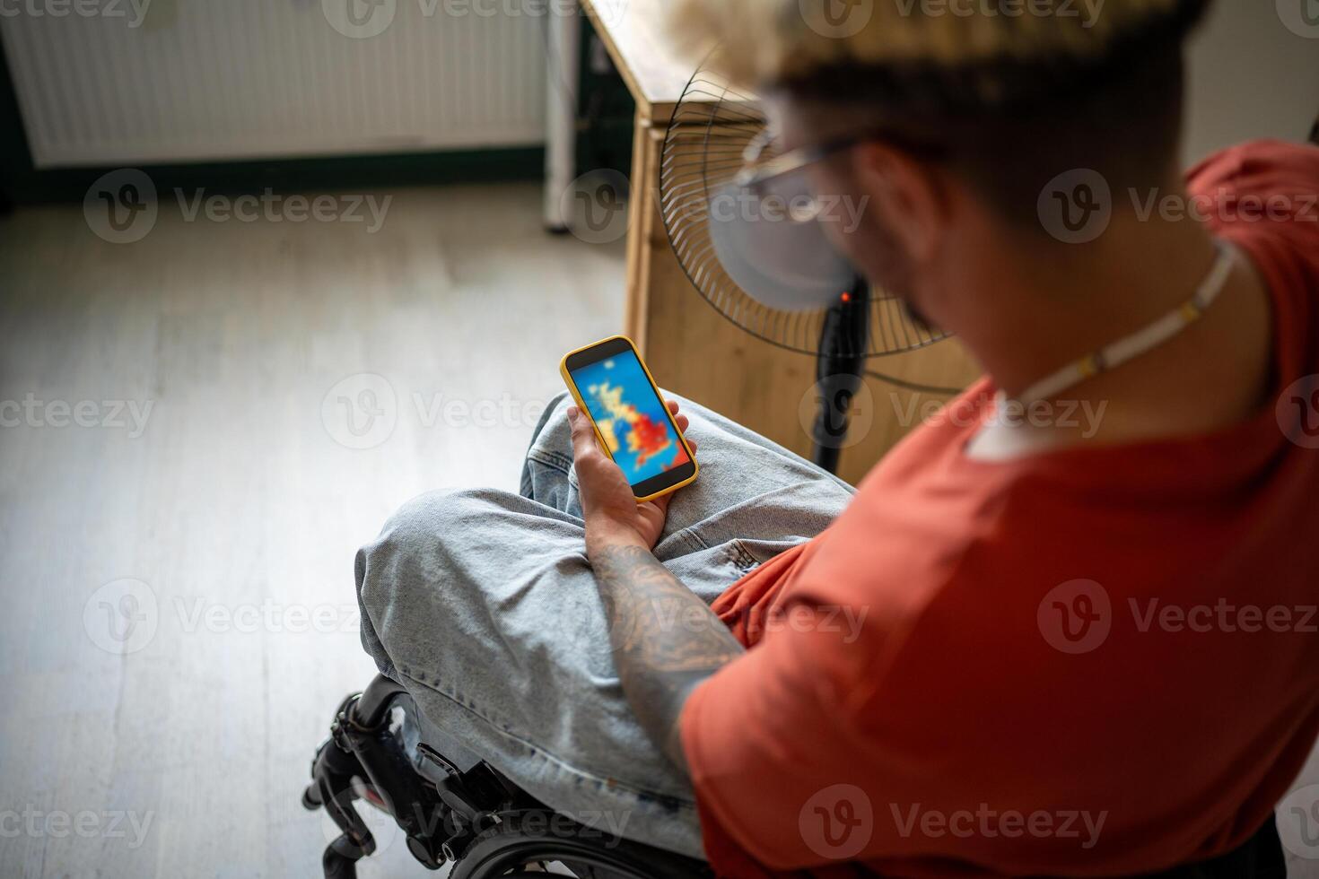 Disabled guy in wheelchair checking weather forecast in mobile app on smartphone at home. Heat wave photo