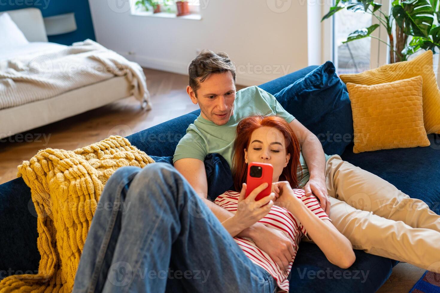 Loving couple resting on couch using smart phone apps. Wife showing interesting website to husband photo