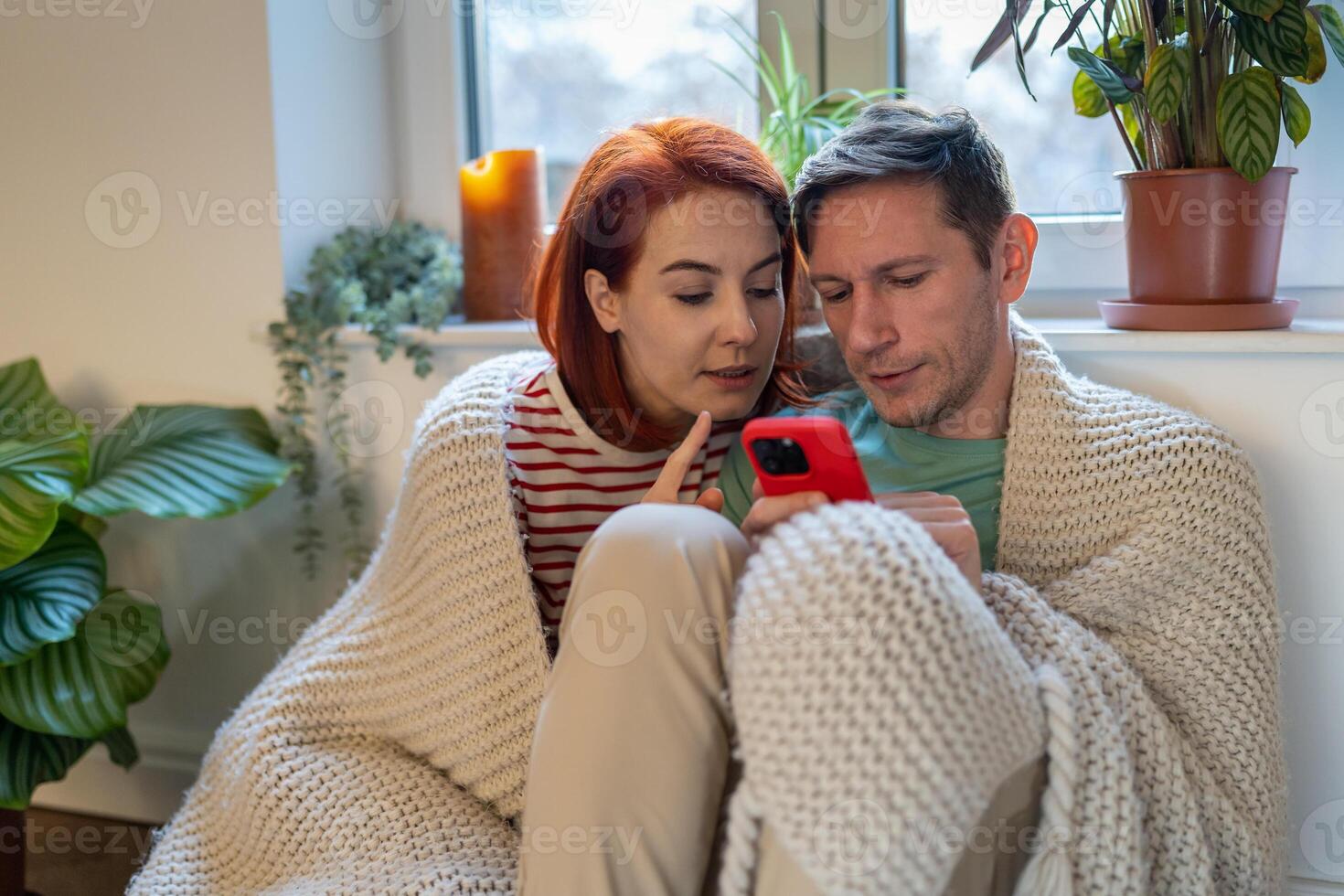 Young married couple sitting on floor, man holding smartphone and discussing order in online store photo