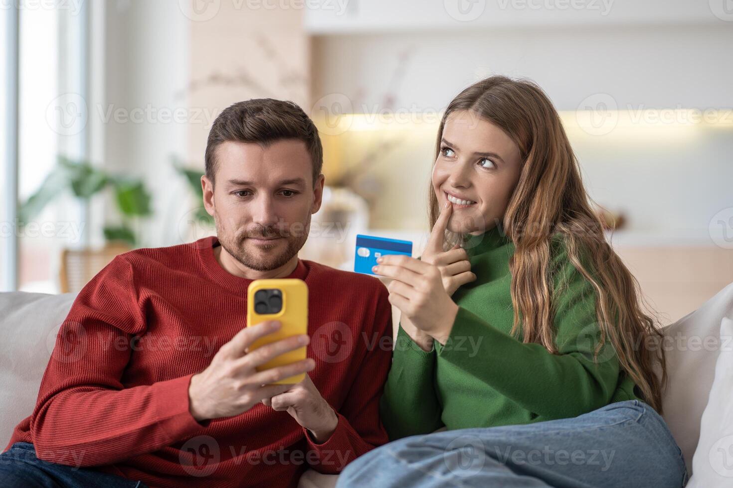 Happy married couple spouses shopping online via internet using smartphone, sitting on couch. photo