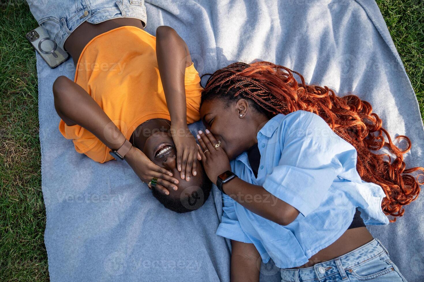 Happy african american girls friends lying on park grass gossips, laugh with eyes covers with palms. photo