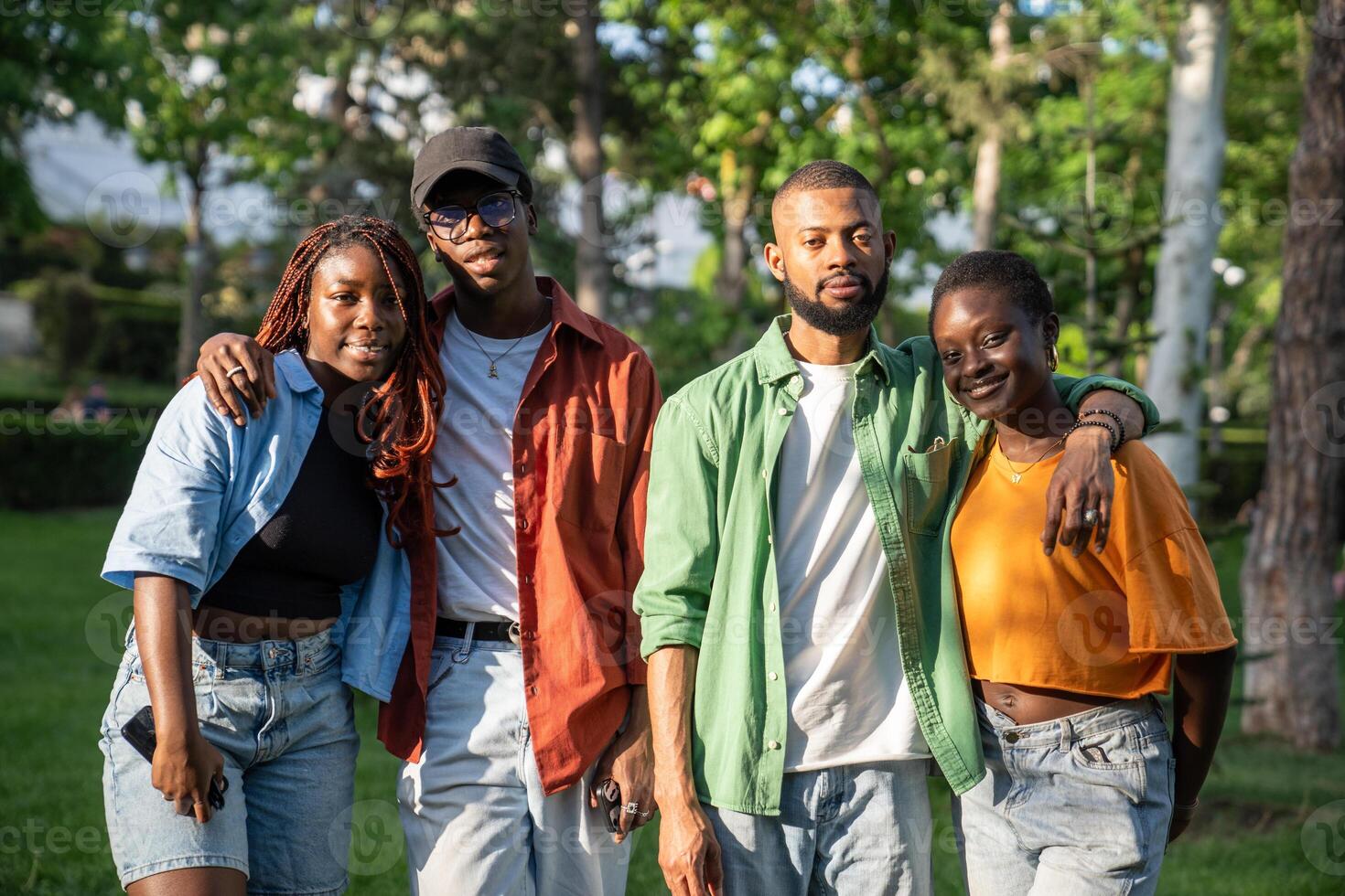 Two African American student couples in love stand in park while walking, smiling looking at camera. photo