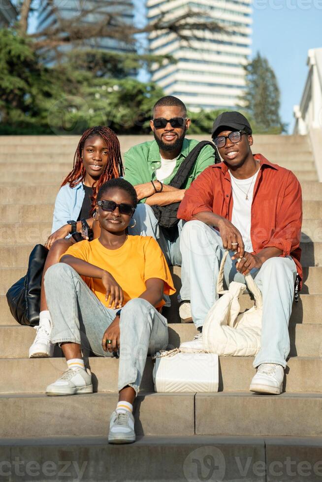 Smiling group of African American friends of students sitting on stairs looking at camera happily. photo
