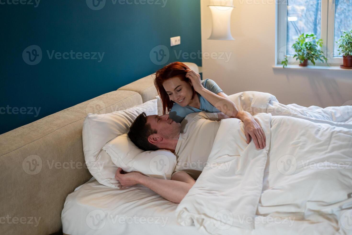 Married couple lying together in bed. Man and woman rest in bed, smiling broadly contentedly. photo