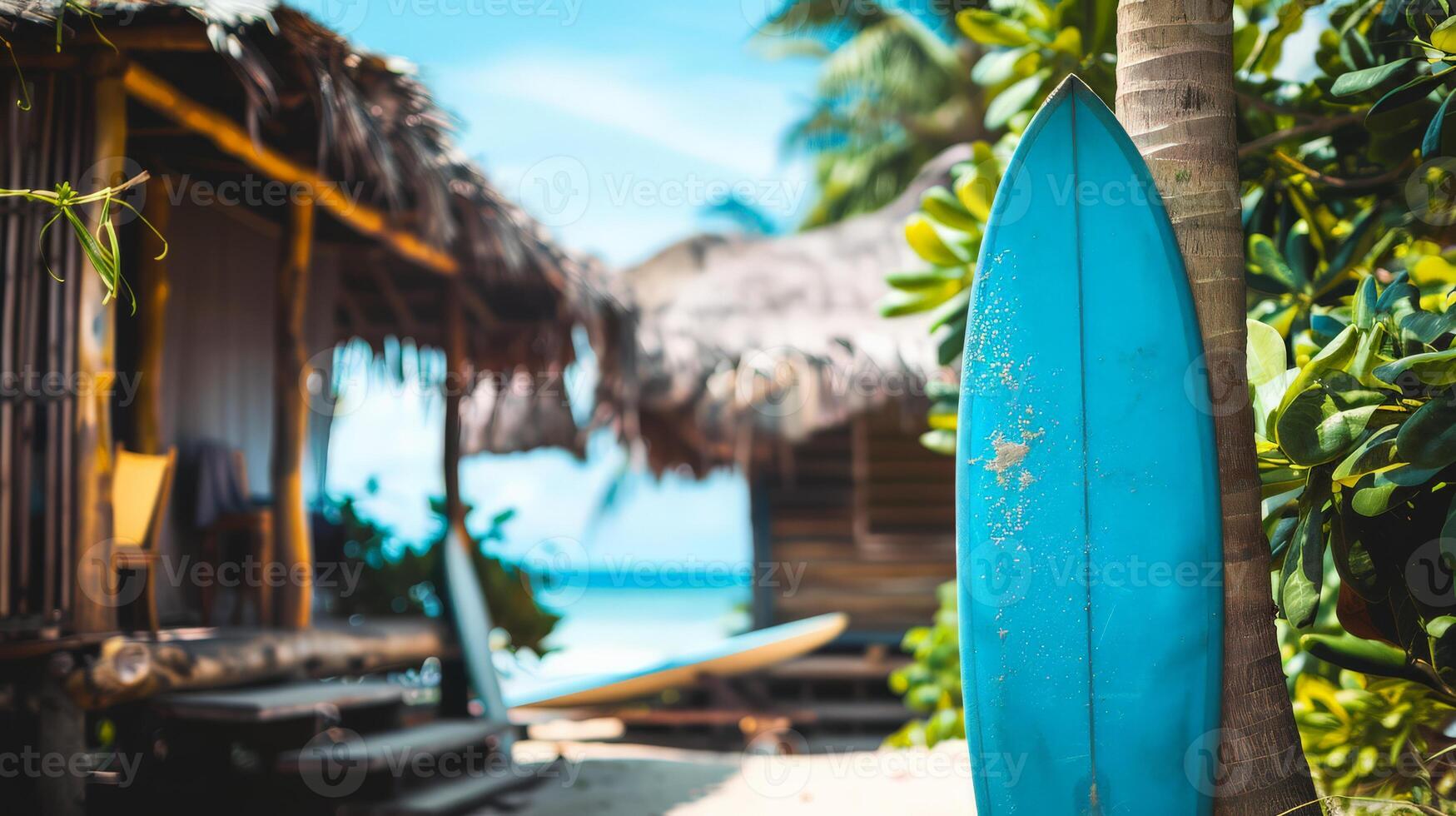 A vibrant surfboard leans against a palm tree by tropical huts photo