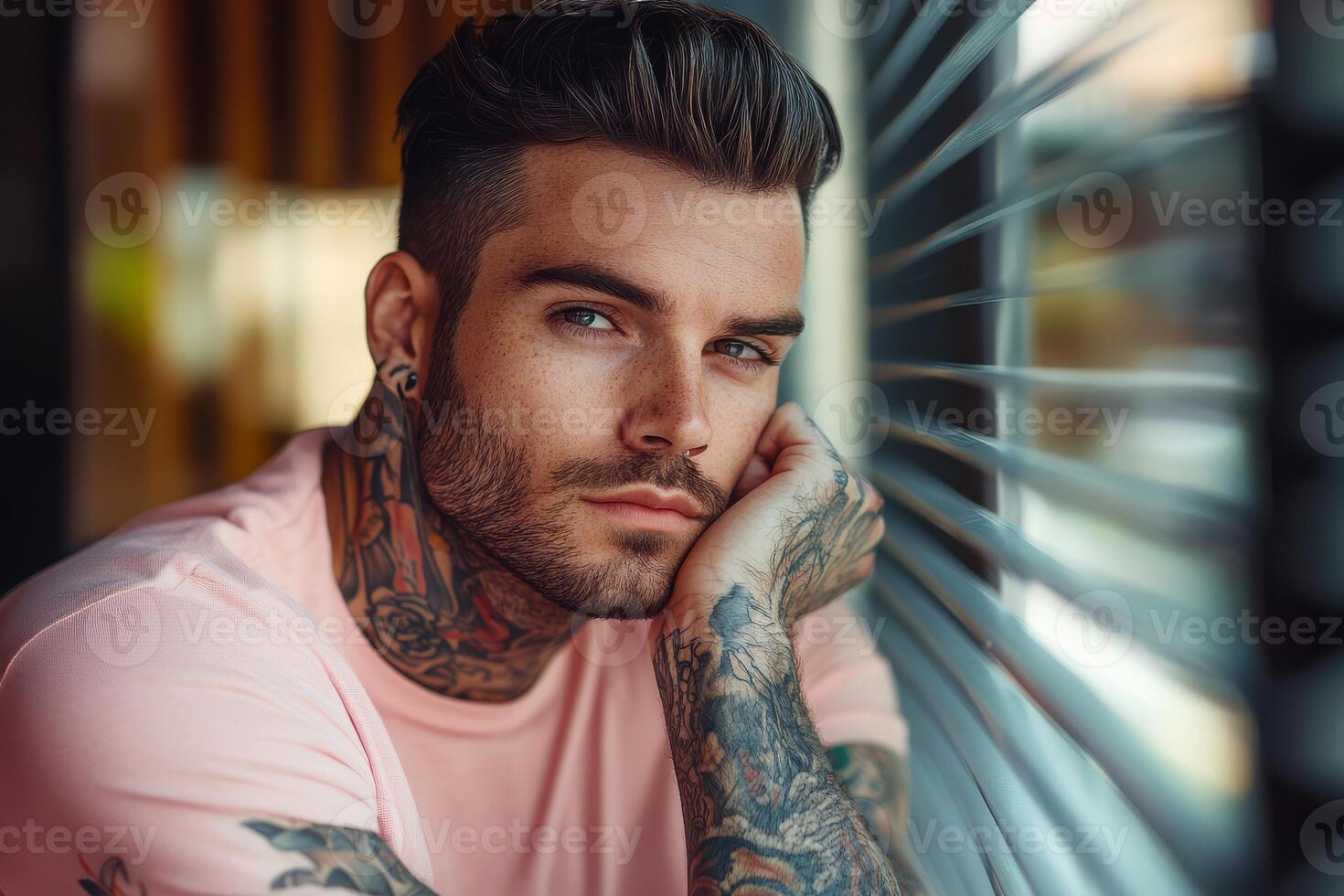 A young man with tattoos rests his chin on his hand, staring out pensively photo