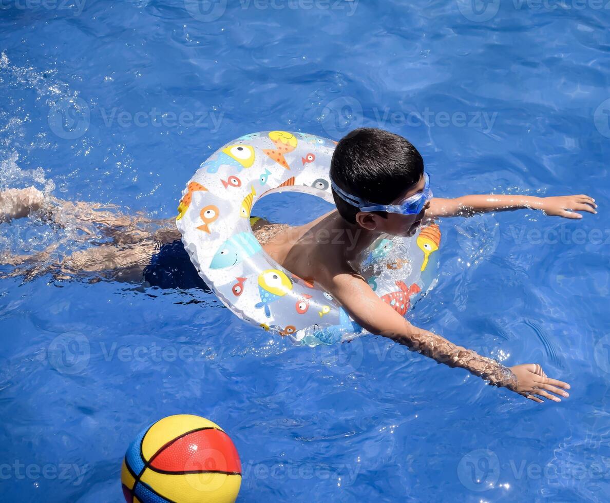 Happy Indian boy swimming in a pool, Kid wearing swimming costume along with air tube during hot summer vacations, Children boy in big swimming pool. photo