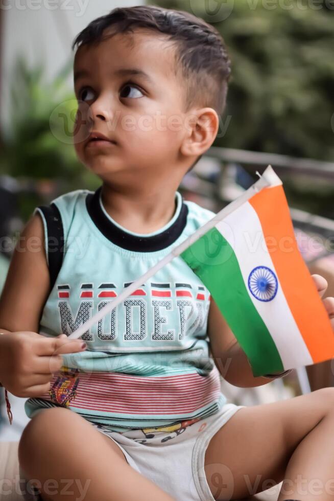 Cute Indian boy holding Indian National Flag in his hangs at home balcony. Bright portrait of happy child sitting on the table with national flag photo