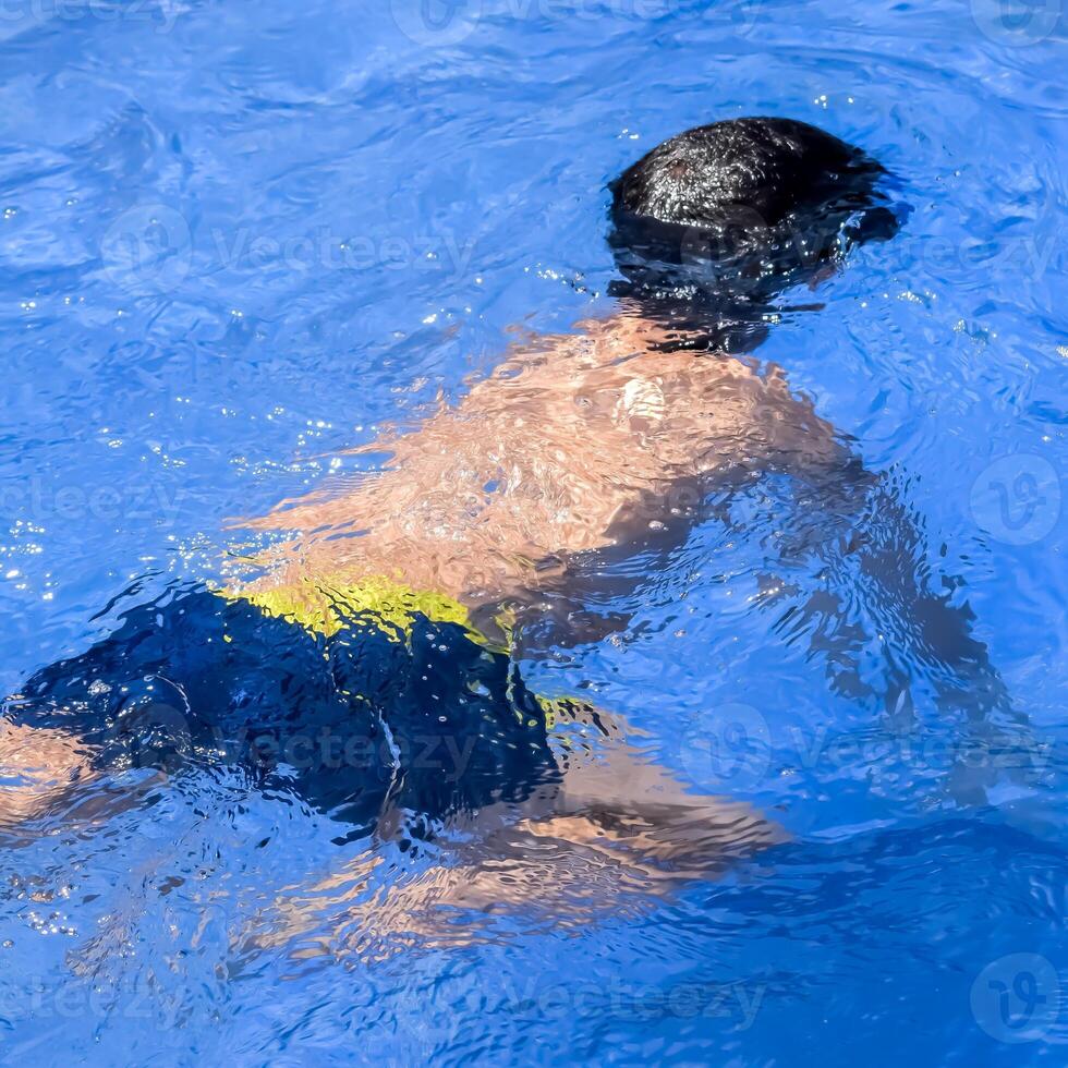 Happy Indian boy swimming in a pool, Kid wearing swimming costume along with air tube during hot summer vacations, Children boy in big swimming pool. photo
