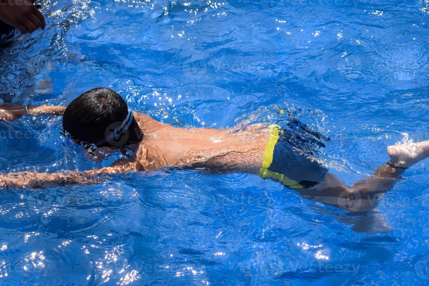 Happy Indian boy swimming in a pool, Kid wearing swimming costume along with air tube during hot summer vacations, Children boy in big swimming pool. photo