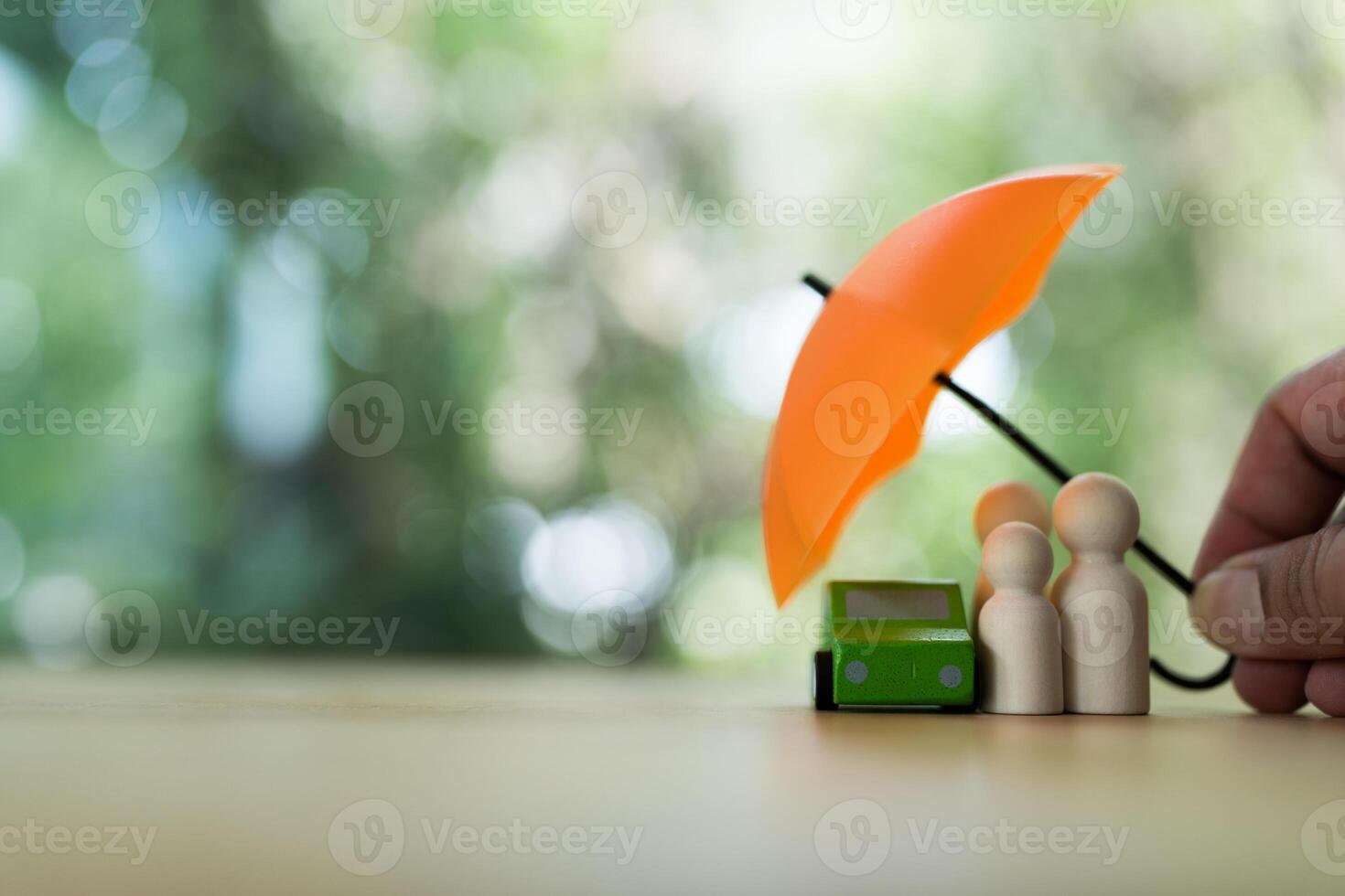 Wood family figures and wood car under umbrella. The insurance agent presents protection photo
