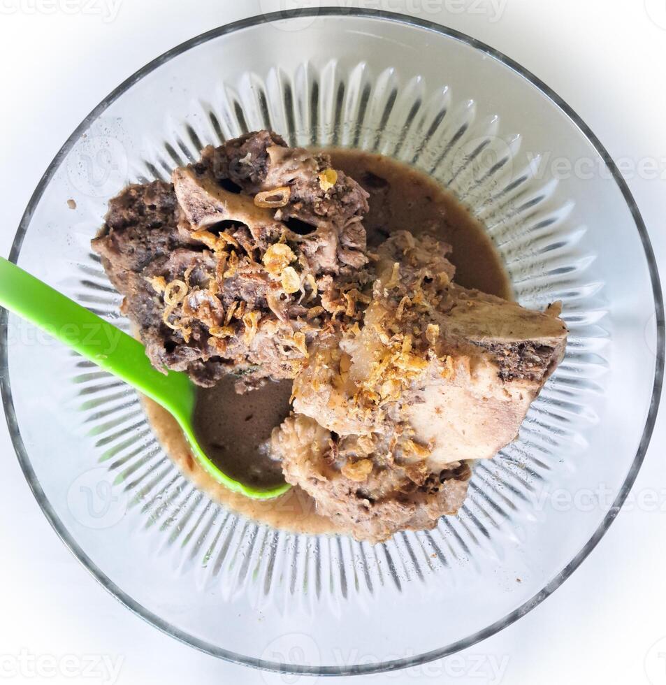 Konro soup is a typical Bugis-Makassar food made from beef ribs or bones wrapped in beef cooked with spices, and served warm, a bowl of kondro soup isolated on a wooden press and white BG photo