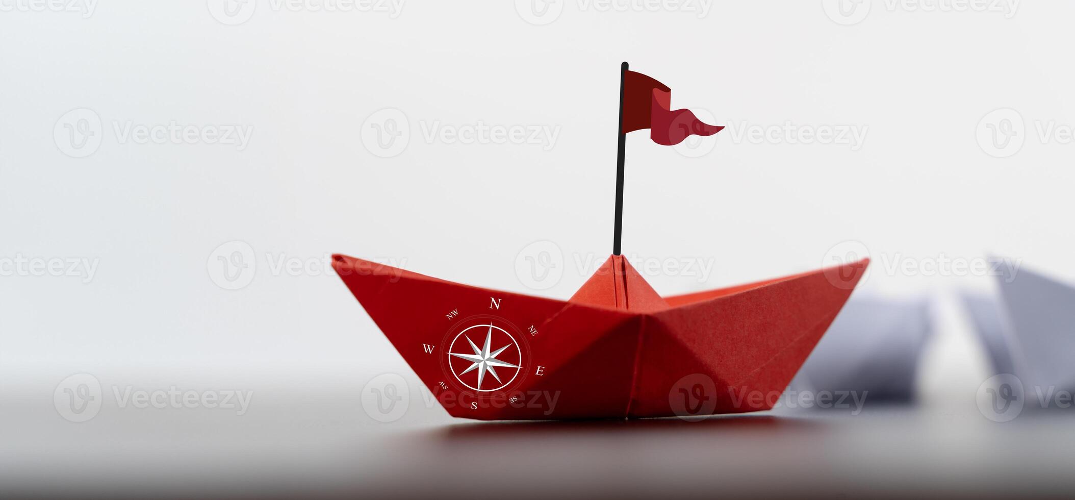 Red paper boat with a compass sails away from a group, representing an entrepreneur taking a new direction photo