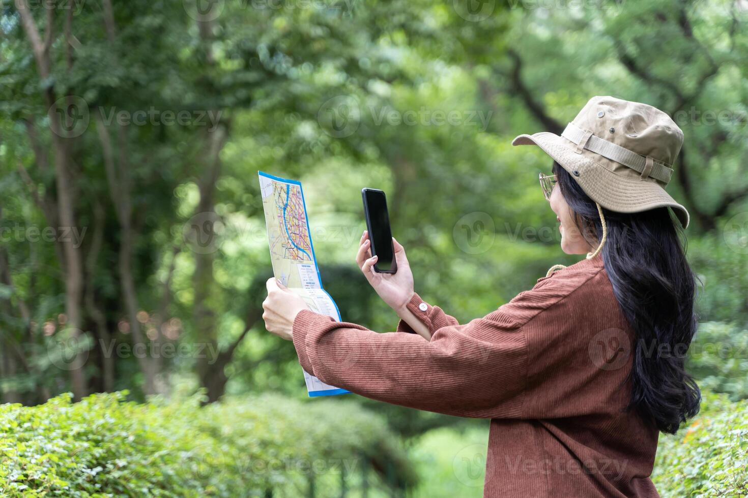 Woman hands with a smartphone and map in the forest background, isolate screen. Happy young woman with a map, smartphone. photo