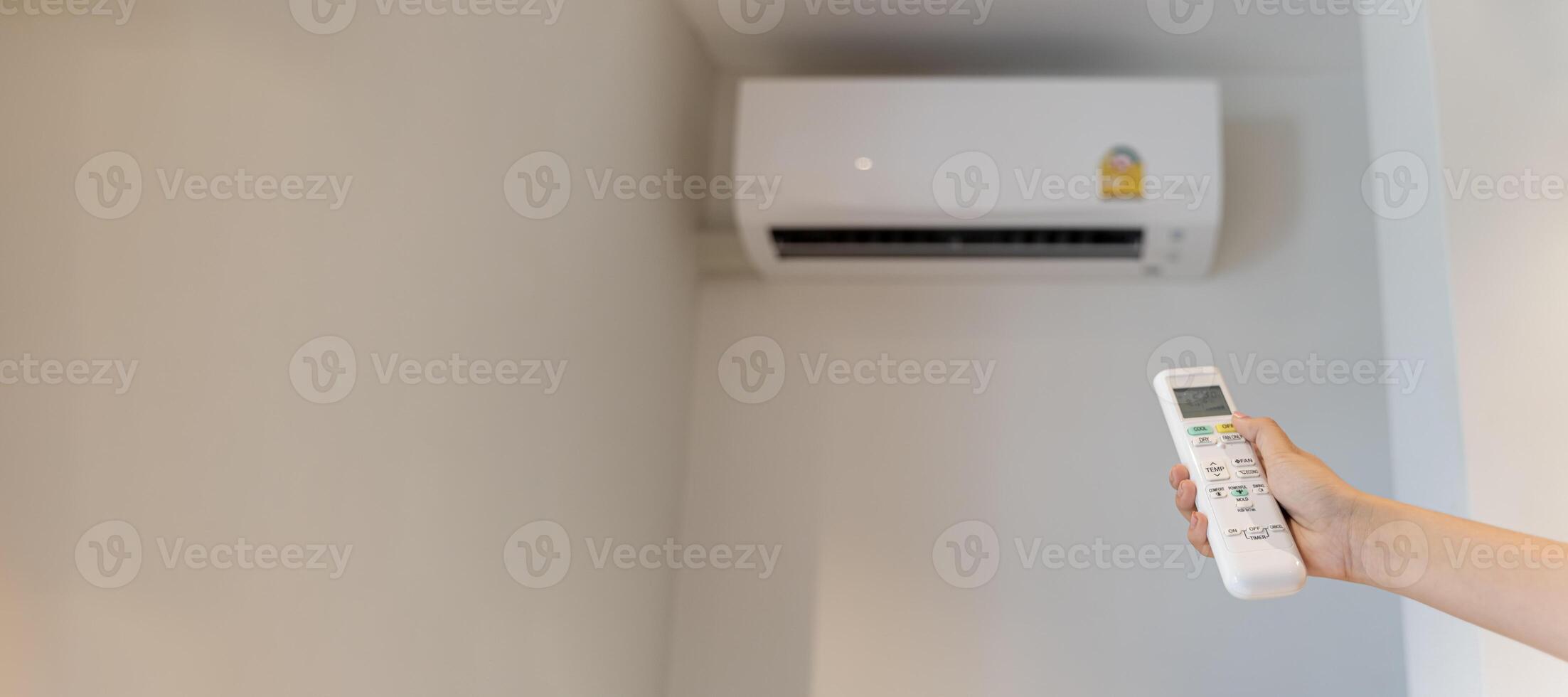 The white air conditioner remote is being used by a human hand to turn on and adjust the air conditioner in a room. Adjusting temperature of air conditioner by remote. photo