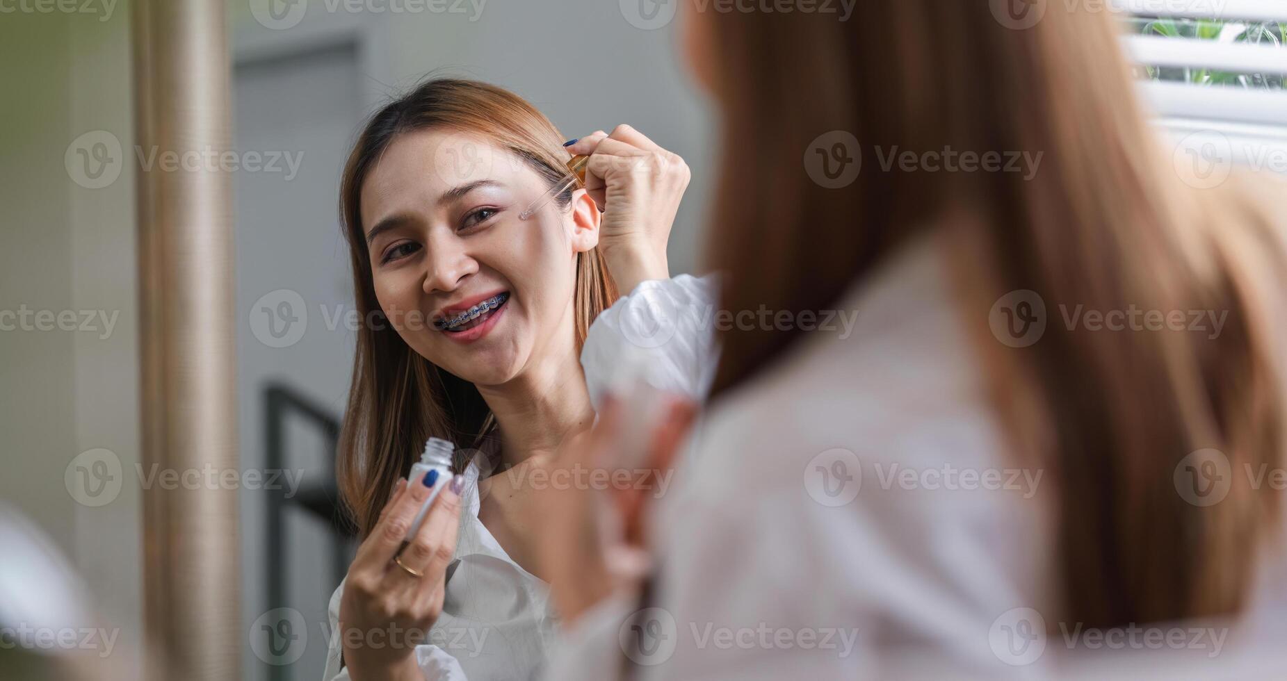 Woman Applying Makeup in the Morning in Front of a Mirror, Smiling and Getting Ready for the Day photo