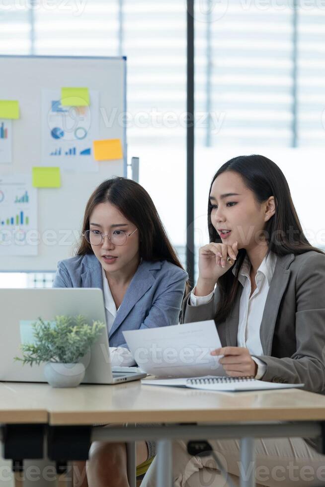 Two Female Accountant Collaborating on Financial Reports in a Modern Office Setting with Charts and Graphs photo